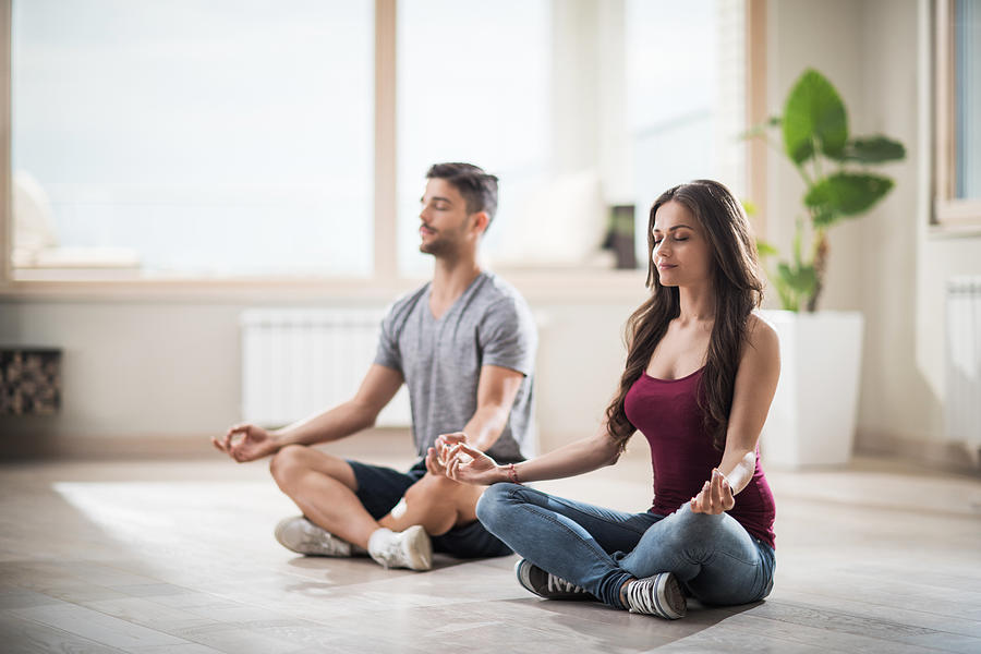 Young couple meditating in Lotus position in their new apartment. Photograph by Skynesher
