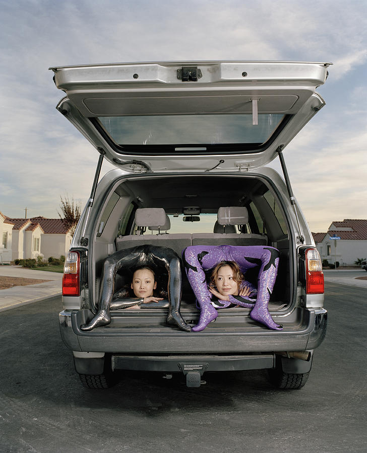 Young female contortionists bending over backwards in vehicle Photograph by Matthias Clamer