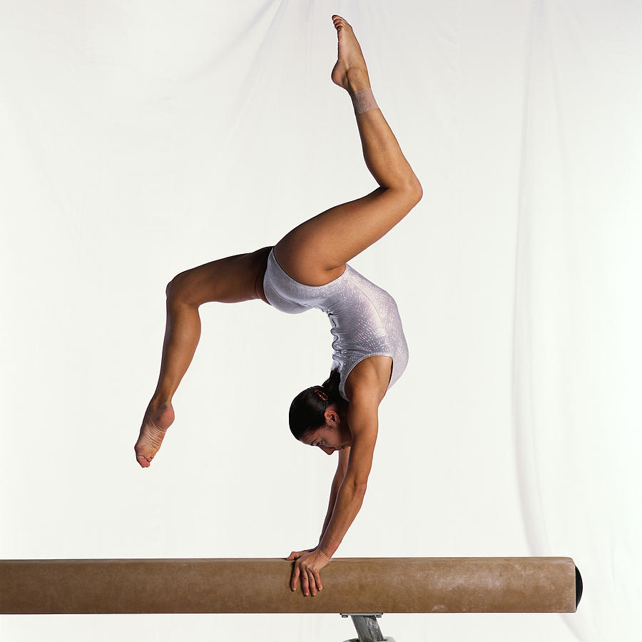 Young female gymnast on balance beam performing exercise, side view. Photograph by Dominique Douieb