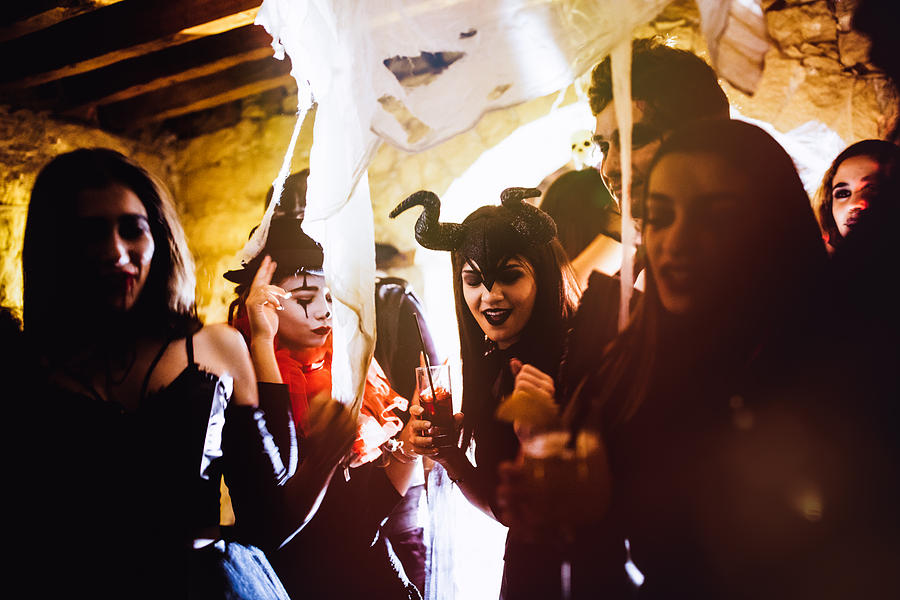 Young friends in Halloween costumes dancing and drinking at party Photograph by Wundervisuals