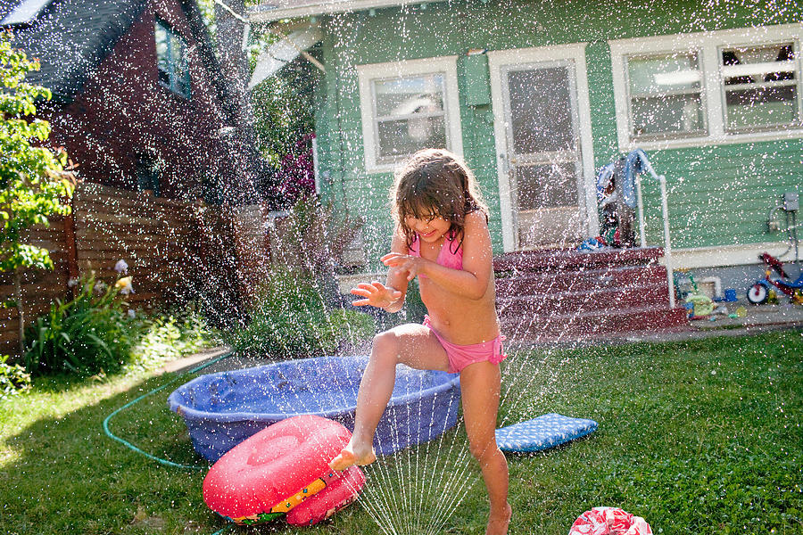Young girl playing in garden sprinkler Photograph by Cultura/Charles Gullung