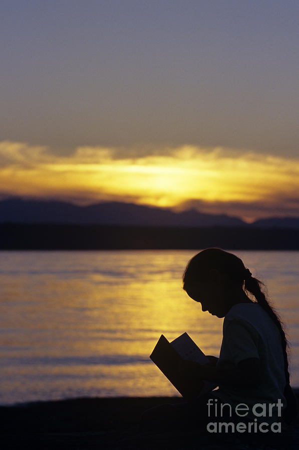 Young girl silhouetted reading a book on the beach at sunset Photograph by Jim Corwin
