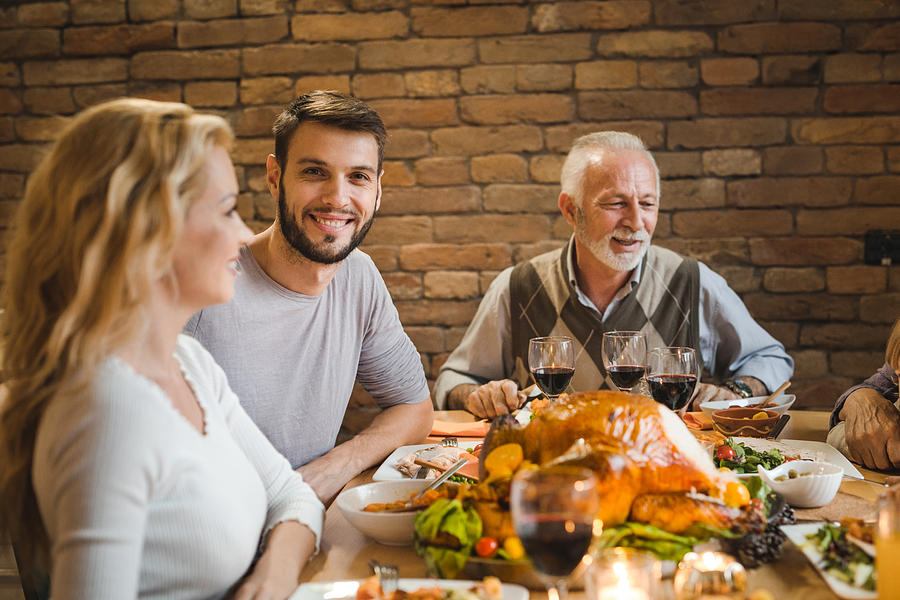 Young happy man enjoying in Thanksgiving dinner with family. Photograph by Skynesher