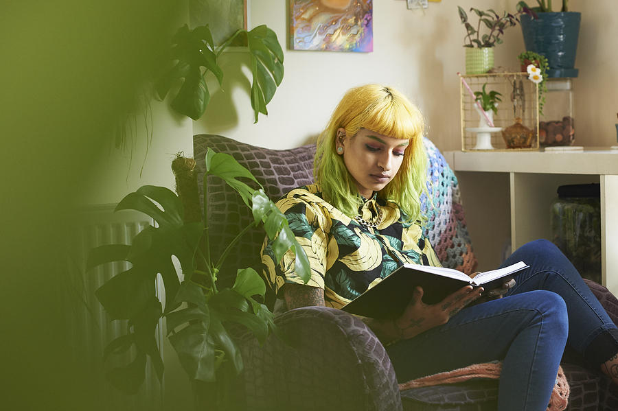 Young hipster woman reading a book in her living room Photograph by Richard Drury