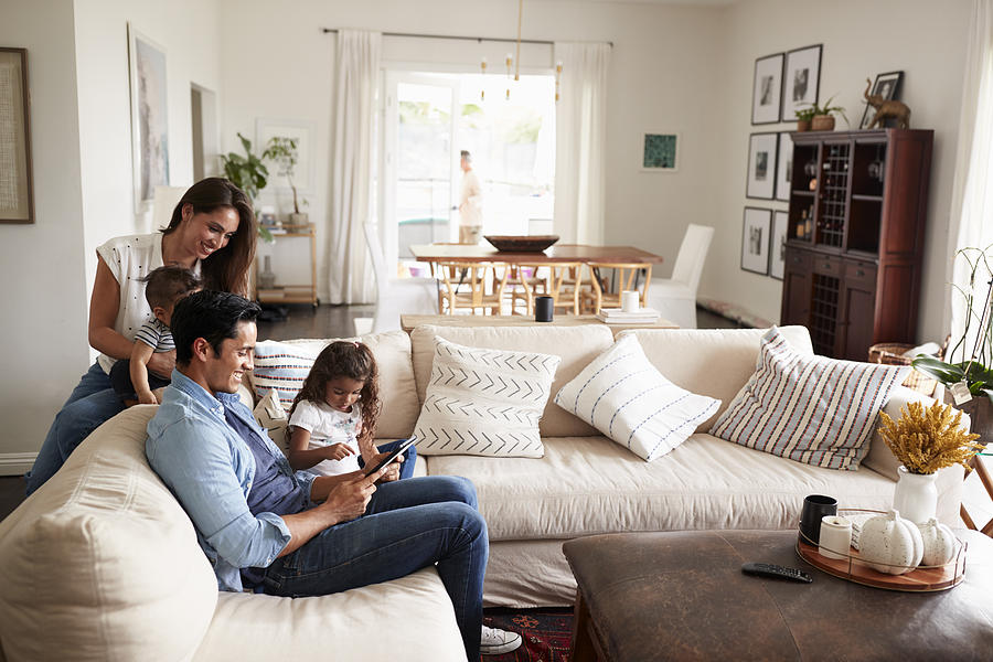 Young Hispanic family sitting on sofa reading a book together in their living room Photograph by Monkeybusinessimages