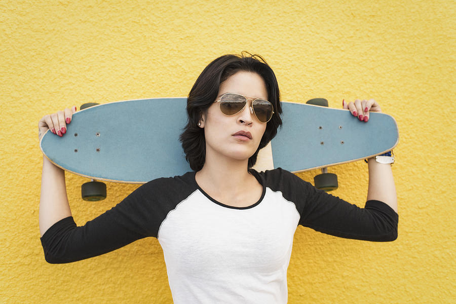 Young Hispanic woman standing near yellow wall with skateboard Photograph by Tony Anderson