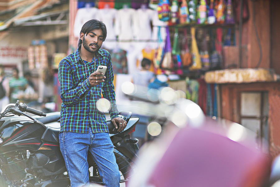 Young Indian man holding phone, with motorbike Photograph by Xavierarnau