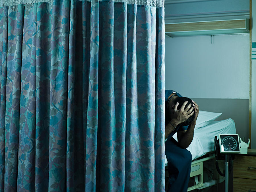 Young male doctor sitting on hospital bed with head in hands Photograph by Image Source