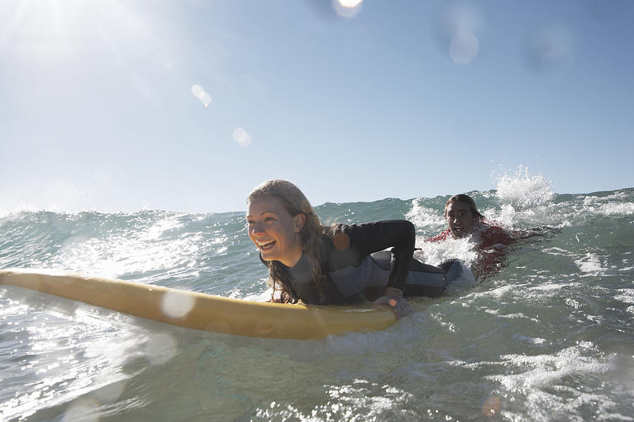 Young man being towed in sea by young woman on surfboard, smiling Photograph by Anthony Ong