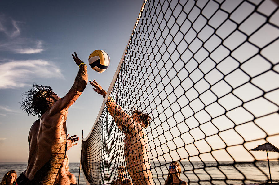 Young man blocking his friend while playing beach volleyball in summer day. Photograph by Skynesher