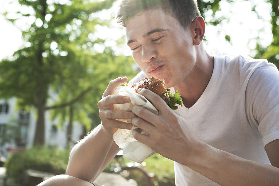 Young man eating hamburger Photograph by Westend61