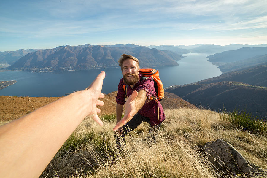 Young man hiking pulls out hand to get assistance Photograph by Swissmediavision