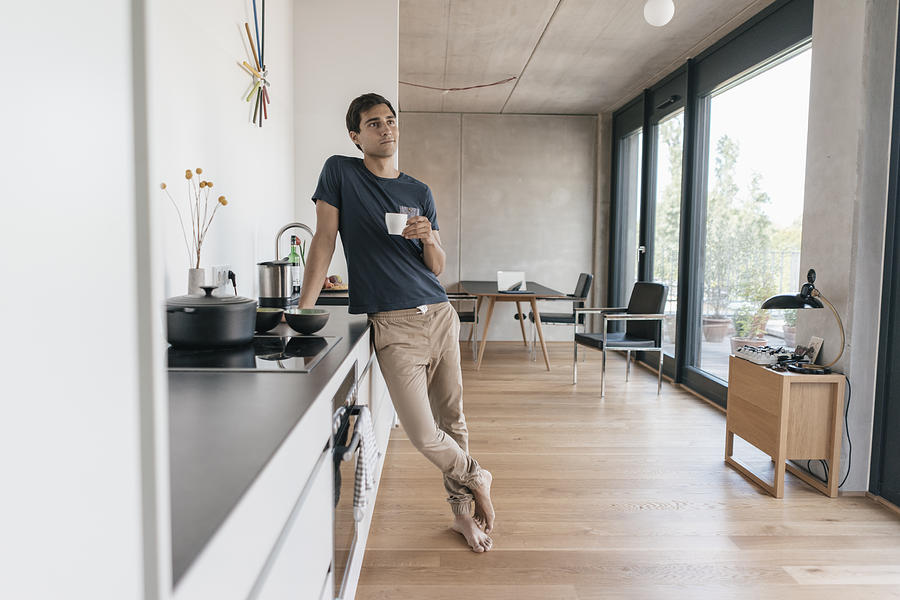 Young man holding cup of coffee in kitchen at home Photograph by Westend61