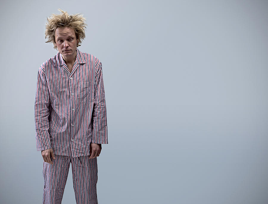 Young man in pajamas looking tired, portrait Photograph by David Zach