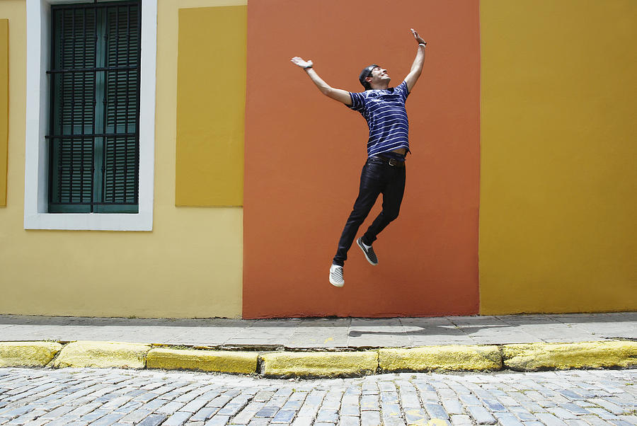 Young man jumping at the roadside Photograph by Hola Images