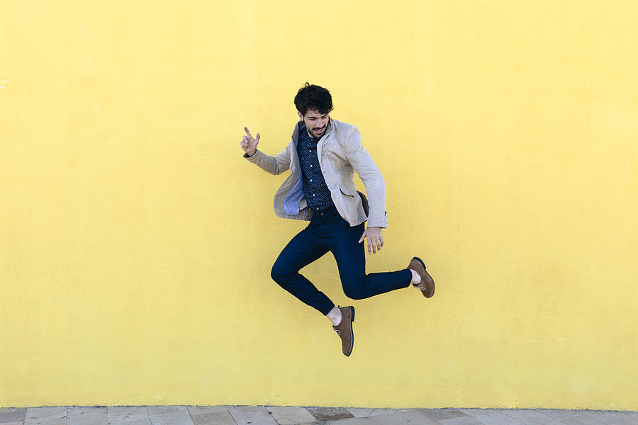Young man jumping in the air in front of yellow wall Photograph by Westend61
