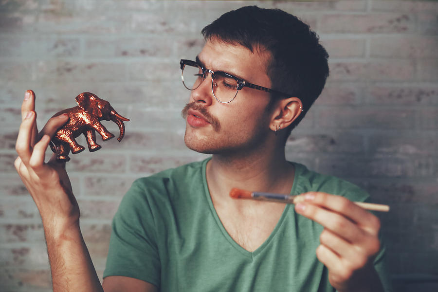 Young man painting plastic elephant figure with copper paint Photograph by Westend61