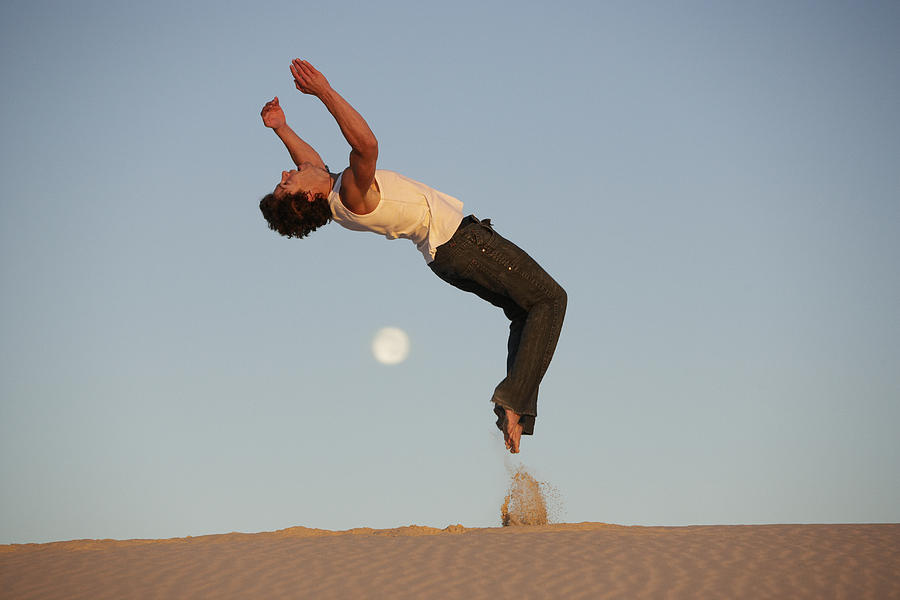 Young man performing backflip in desert, side view, dusk Photograph by Justin Pumfrey