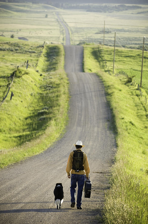 Young man walking with dog down rural road, rear view Photograph by Zia Soleil