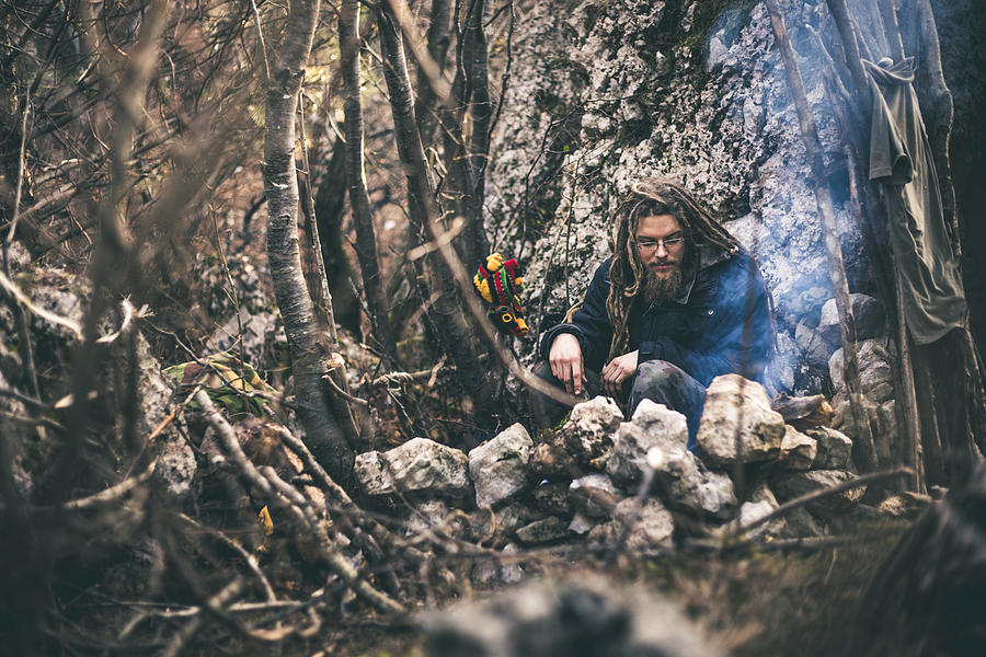 Young Man With Dreadlocks Sitting By a Fireplace in Nature Photograph by CasarsaGuru