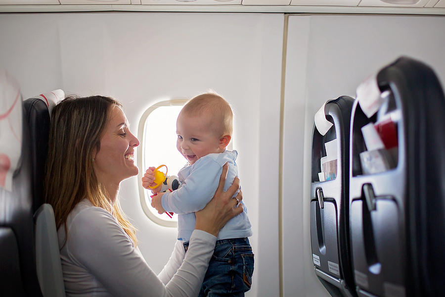 Young mom, playing and breastfeeding her toddler boy on board of aircraft Photograph by Tatyana_tomsickova