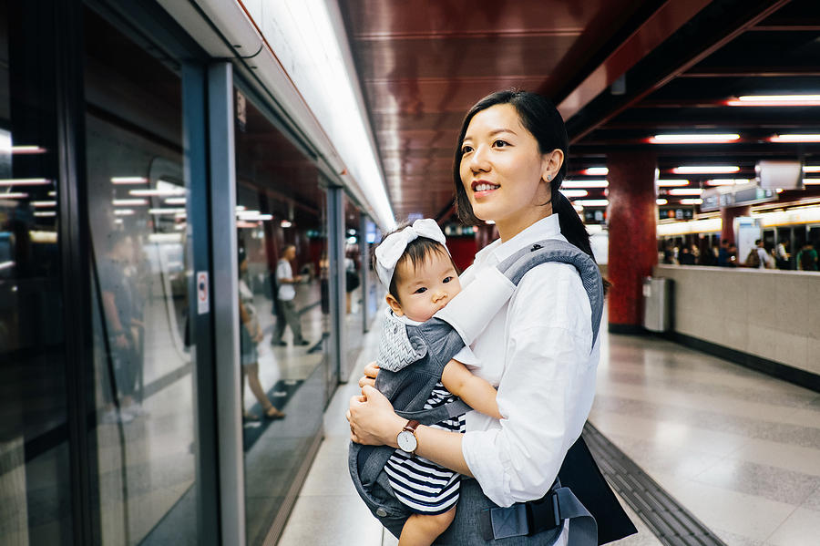 Young mother carrying cute baby girl waiting for subway in subway station Photograph by D3sign