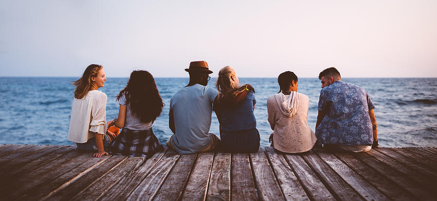 Young multi-ethnic couples and friends sitting on wooden jetty together Photograph by Wundervisuals