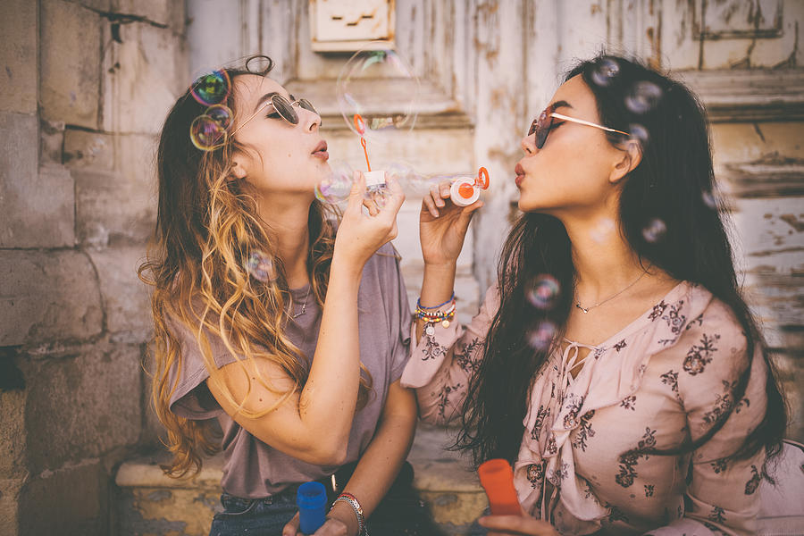 Young multi-ethnic women blowing bubbles in old city street Photograph by Wundervisuals