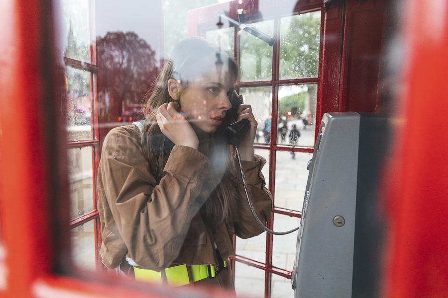 Young woma nmaking a call from a red phone booth in the city, London, UK Photograph by Westend61