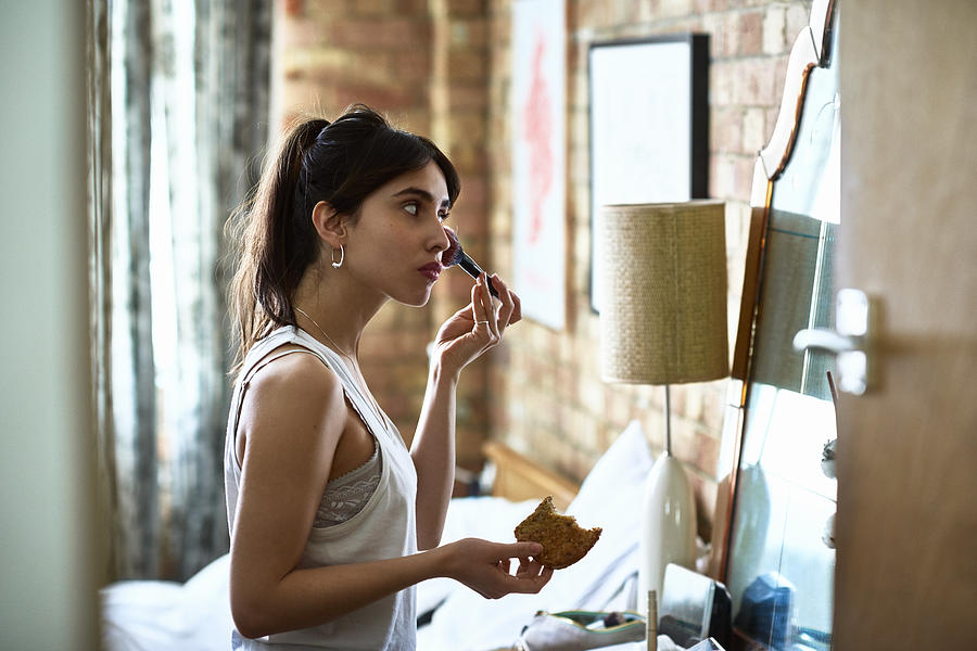 Young woman applying blusher with make up and holding toast Photograph by 10000 Hours