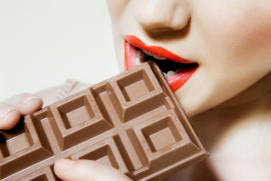 Young woman biting chocolate, close up Photograph by Image Source