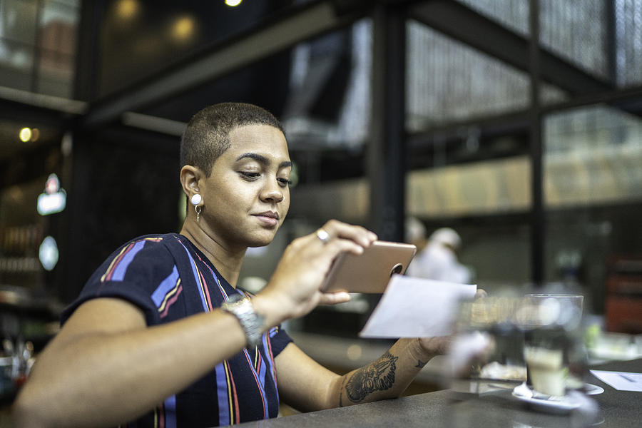 Young woman depositing check by phone in the cafe Photograph by FG Trade