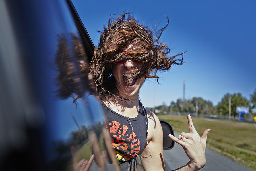 Young woman hanging out car window Photograph by Brook Pifer
