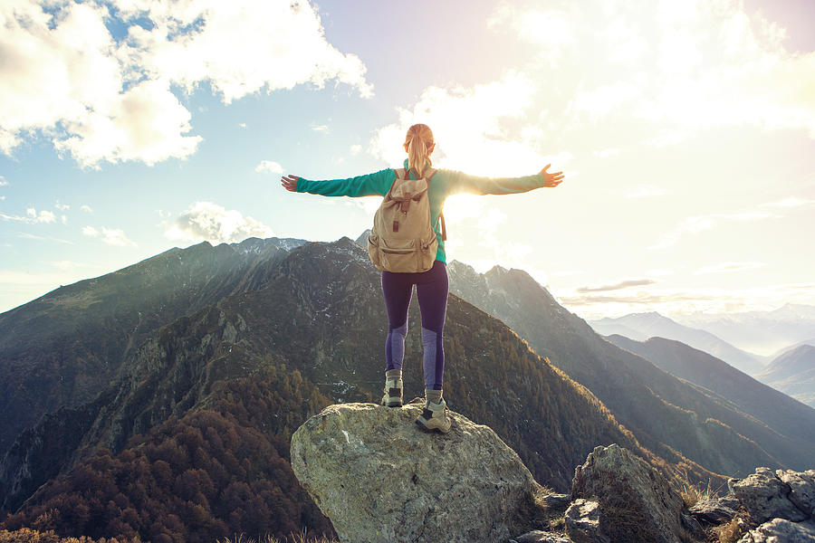 Young woman hiking reaches the mountain top, outstretches arms Photograph by Swissmediavision
