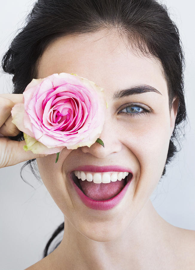 Young woman holding rose to her face, laughing Photograph by Dimitri Otis