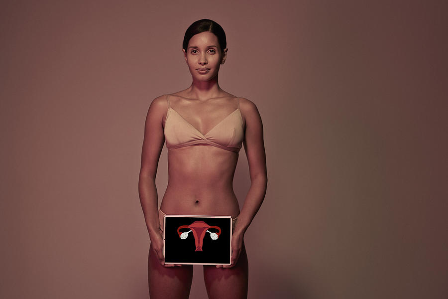 Young woman holding tablet in front of body to show womb & ovaries Photograph by Klaus Vedfelt