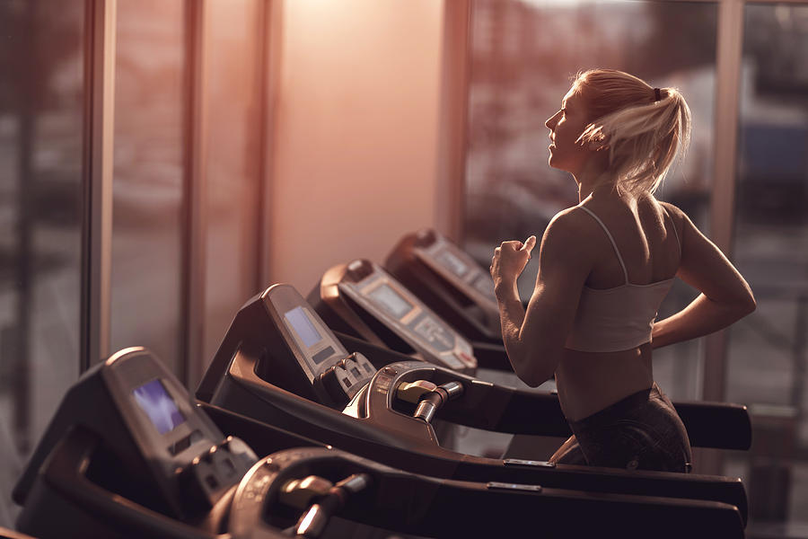 Young woman jogging on a treadmill in a gym. Photograph by Skynesher