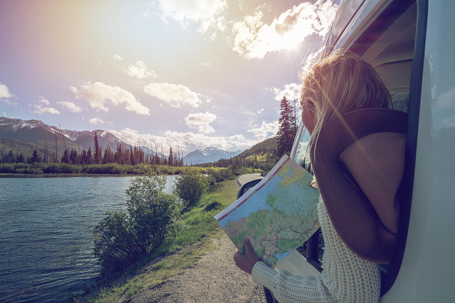 Young woman looks at road map near mountain lake Photograph by Swissmediavision