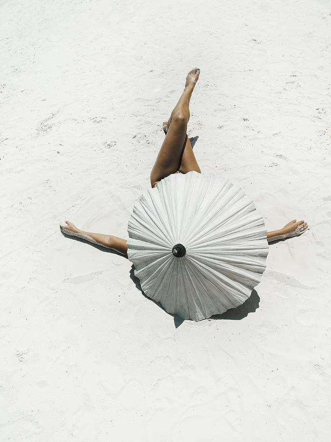 Young woman lying on back protected by parasol on beach, rear view Photograph by David Trood