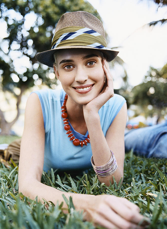 Young Woman Lying on Grass in a Park Wearing a Trilby Hat Photograph by Digital Vision.