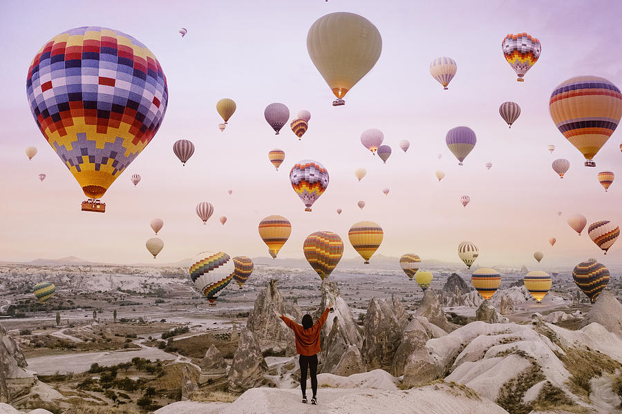Young woman on a background of flying balloons at sunrise in Cappadocia Photograph by Anna Shvets