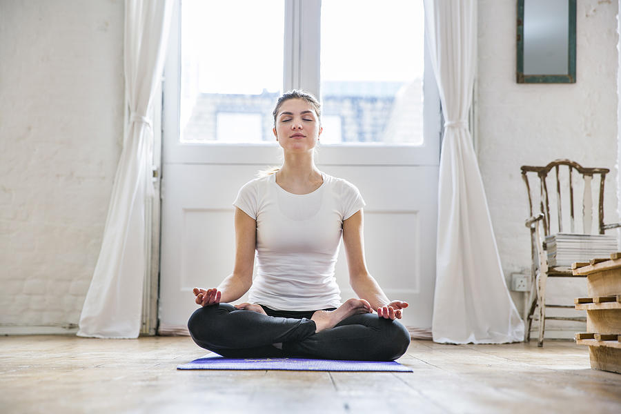 Young woman practicing yoga lotus position in apartment Photograph by Tom Dunkley