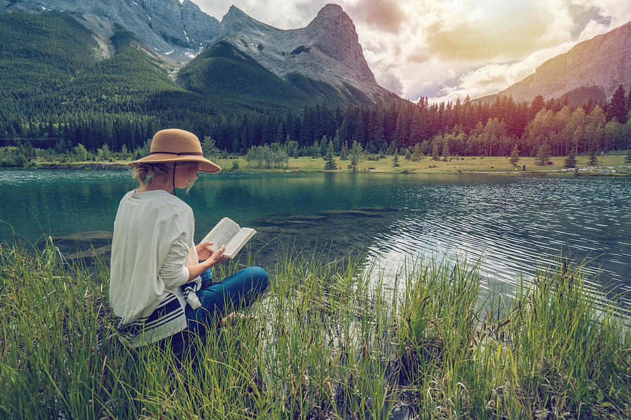 Young woman reading a book by the lake Photograph by Swissmediavision