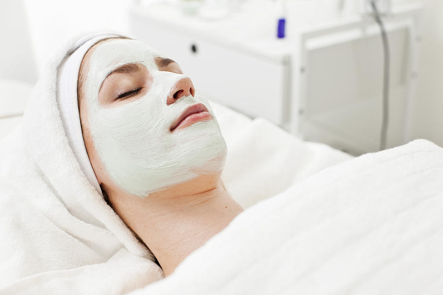 Young woman relaxing on massage table with facial mask at beauty spa Photograph by Maskot