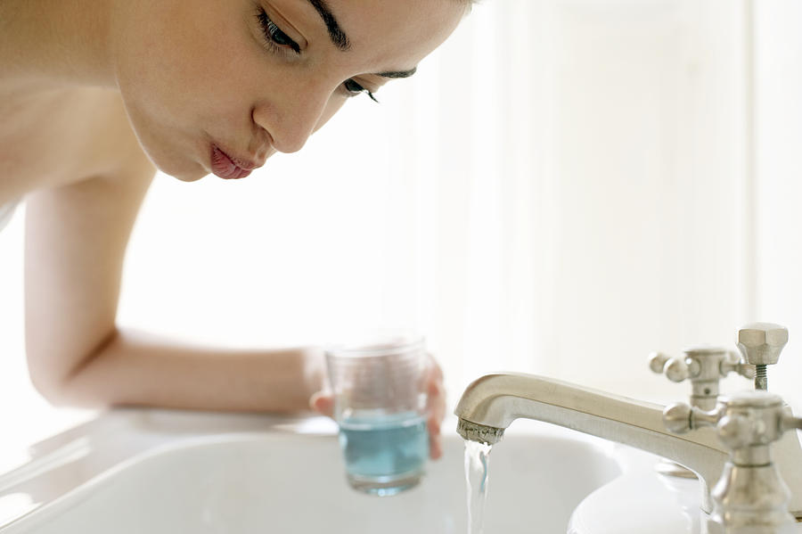 Young woman rinsing mouth, leaning over sink, close-up Photograph by Christopher Robbins