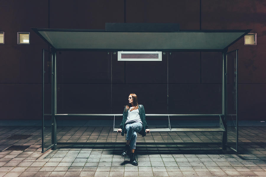 Young woman sitting at bus stop at night Photograph by Eugenio Marongiu