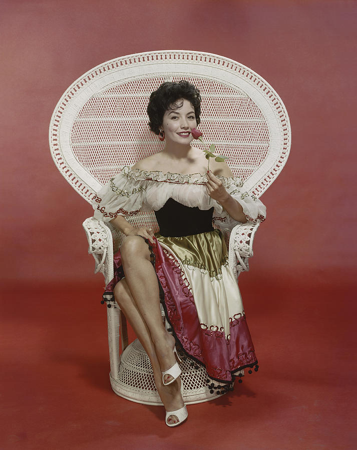 Young woman sitting on chair holding rose, smiling, portrait Photograph by Tom Kelley Archive