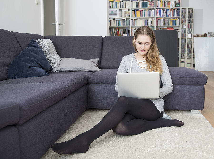 Young woman sitting on the floor of living room using laptop Photograph by Westend61