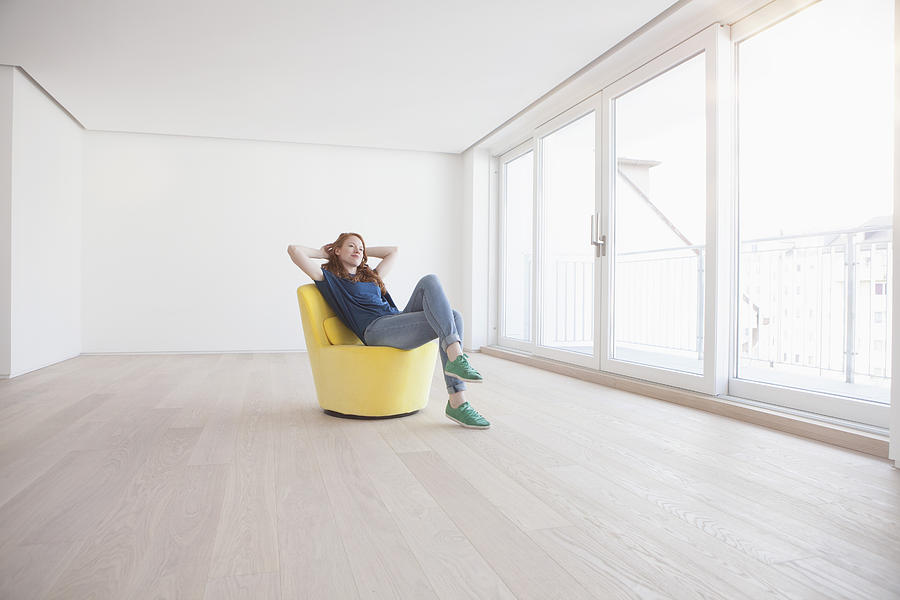 Young woman sitting on yellow armchair in her empty living room Photograph by Westend61