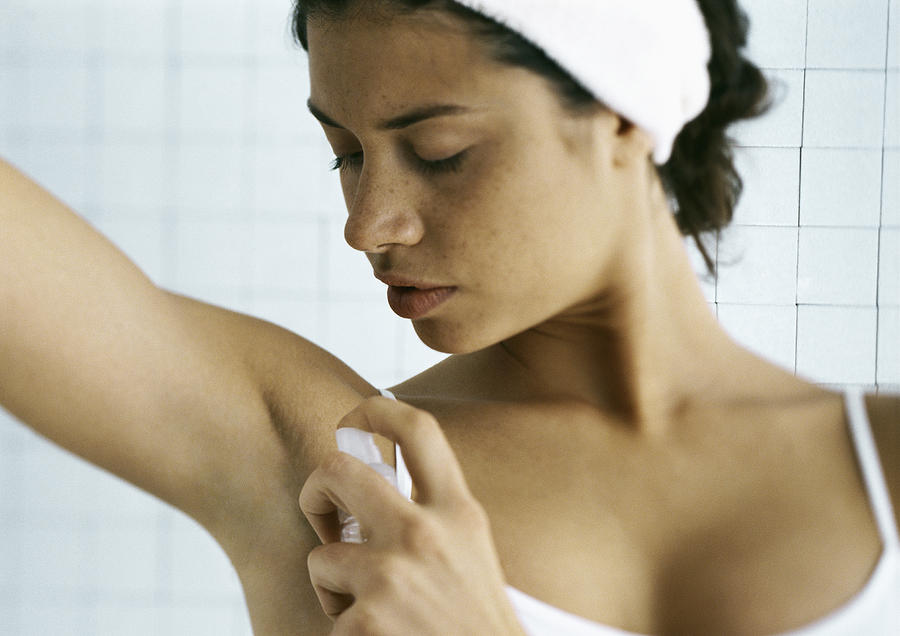 Young woman spraying underarm, head and shoulders Photograph by Frederic Cirou